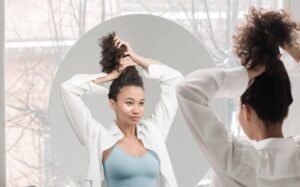 Tjej med lockigt hår som står framför en spegel och sätter upp sitt hår.