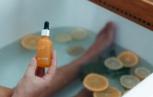 Bild på en person i ett badkar med citrusfrukter i vattnet som håller i ett c-vitamin serum.